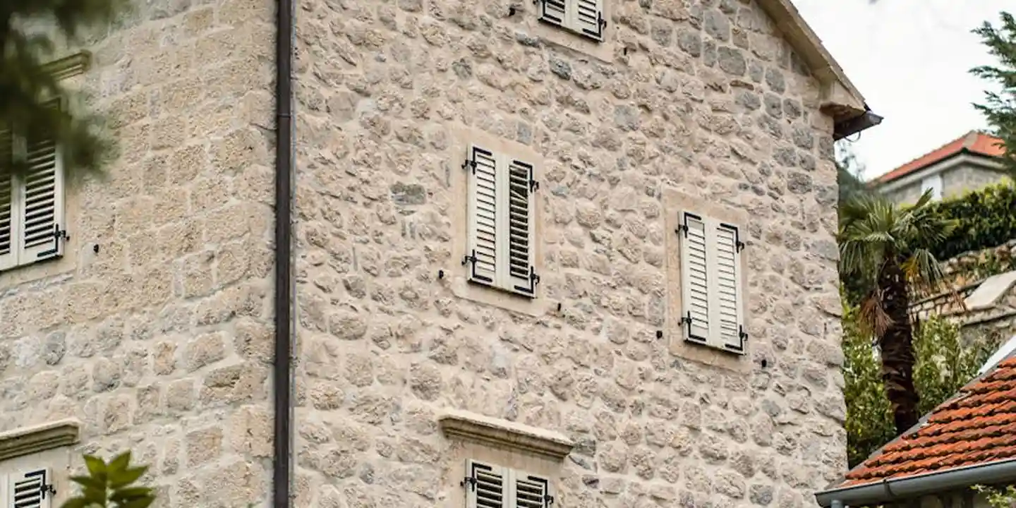 Stone house facade with shuttered windows and a red-tiled roof, highlighting exterior roofing materials.