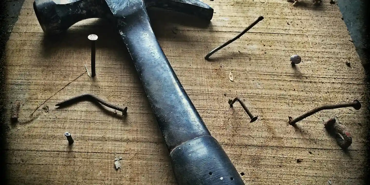 Hammer and scattered roofing nails on a wooden work surface.