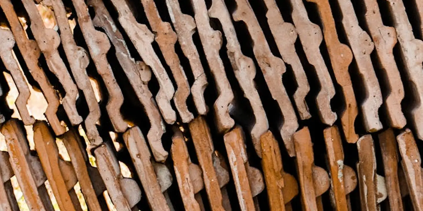 Close-up of overlapping metal roof shingles with weathered, uneven edges.