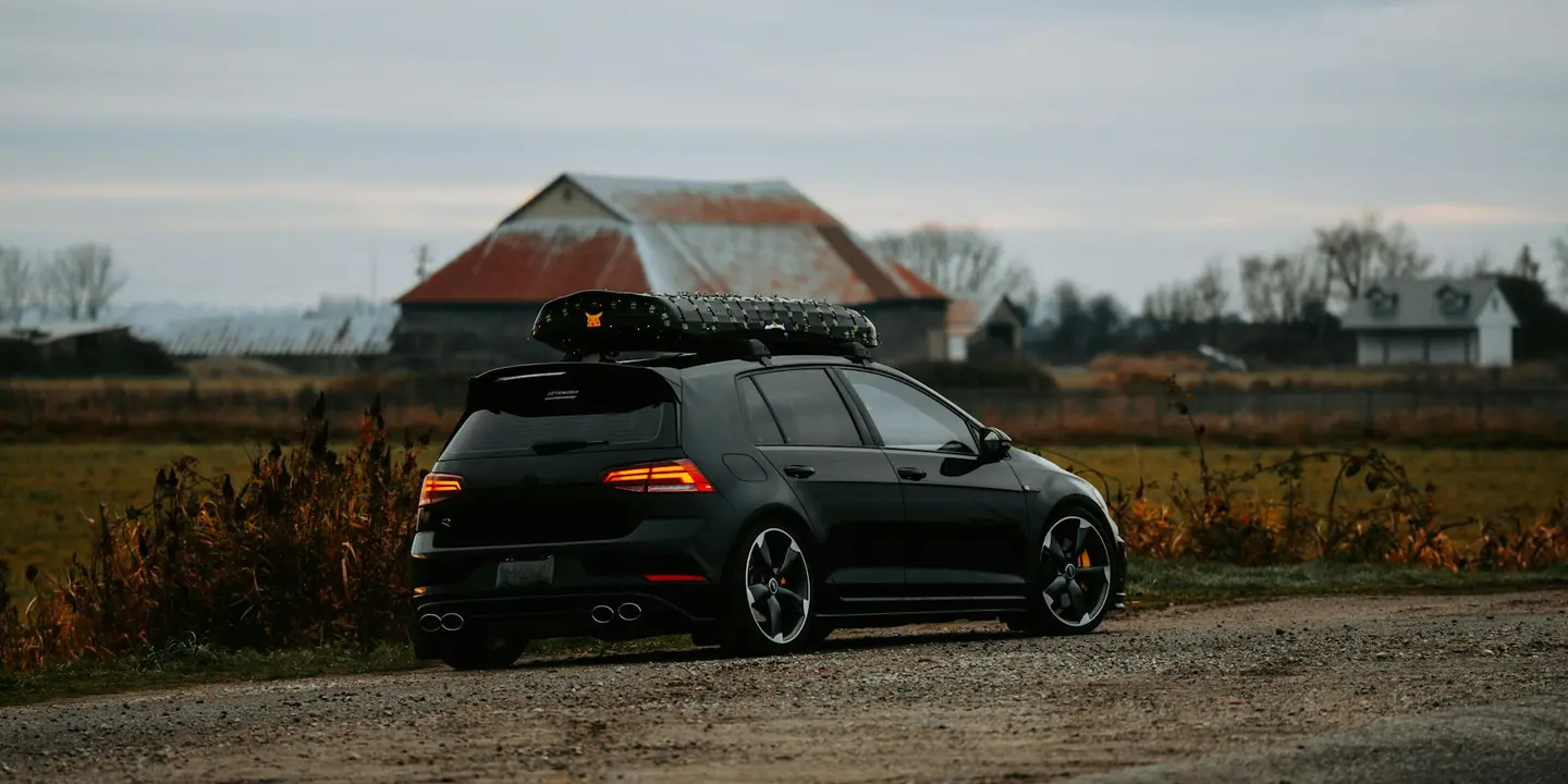 Black SUV with a roof rack parked on a rural gravel road with a barn in the background