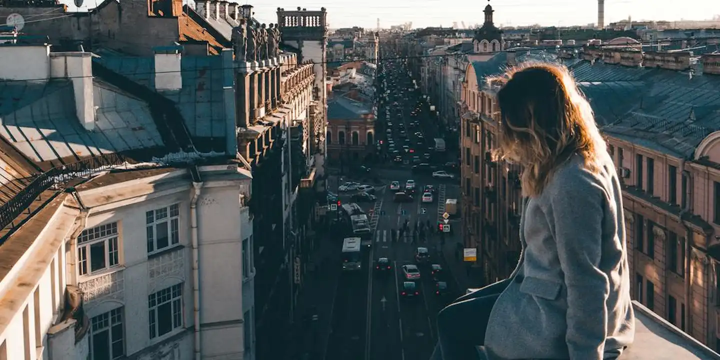 A person stands on a rooftop overlooking a dense city street with buildings and traffic below.