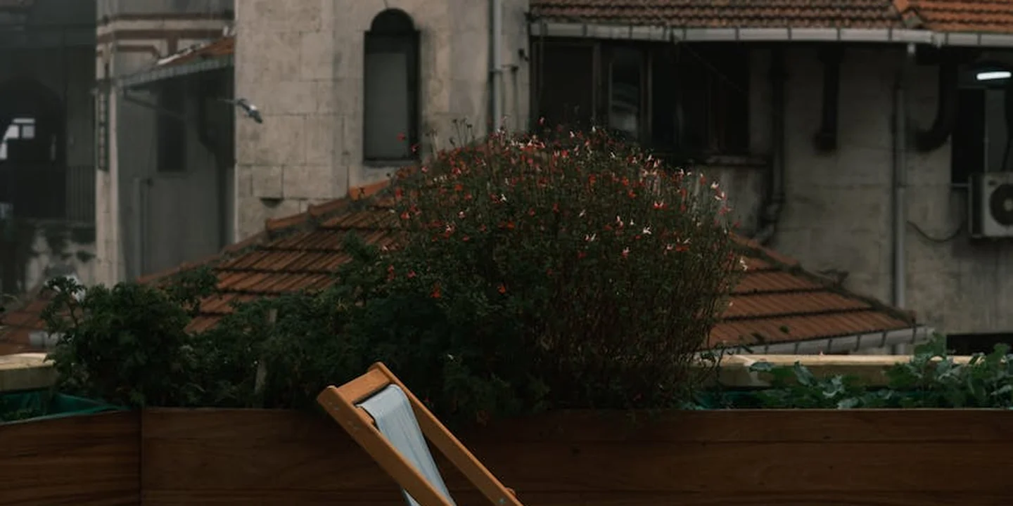 Rooftop deck or balcony edge with wooden planks and a low railing in an urban setting, showing clutter and potential safety hazards