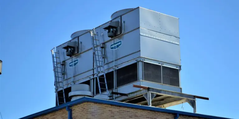 Two rooftop air conditioning units mounted on a dark metal roof against a clear blue sky.