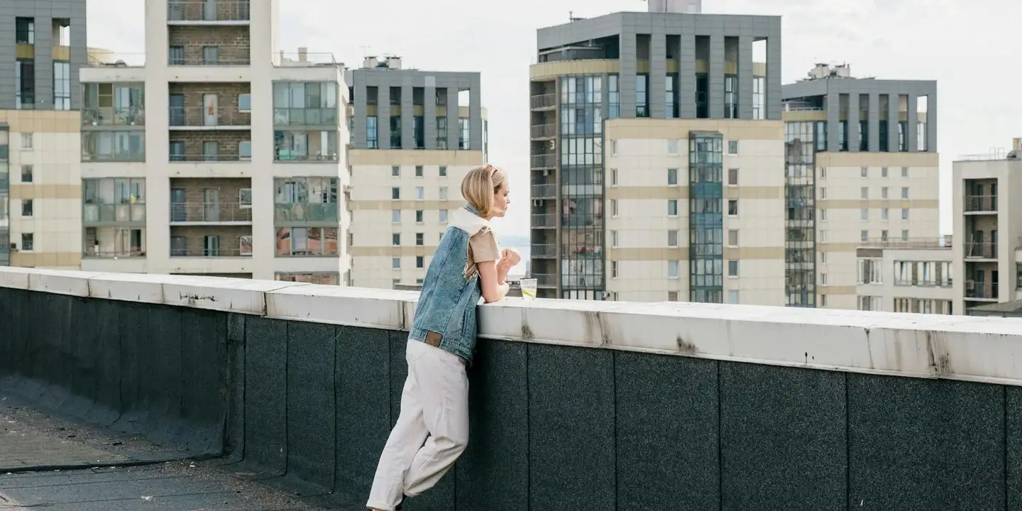 A person leaning on a rooftop railing with a cityscape in the background, illustrating potential leak-prone junctions along a residential roof.
