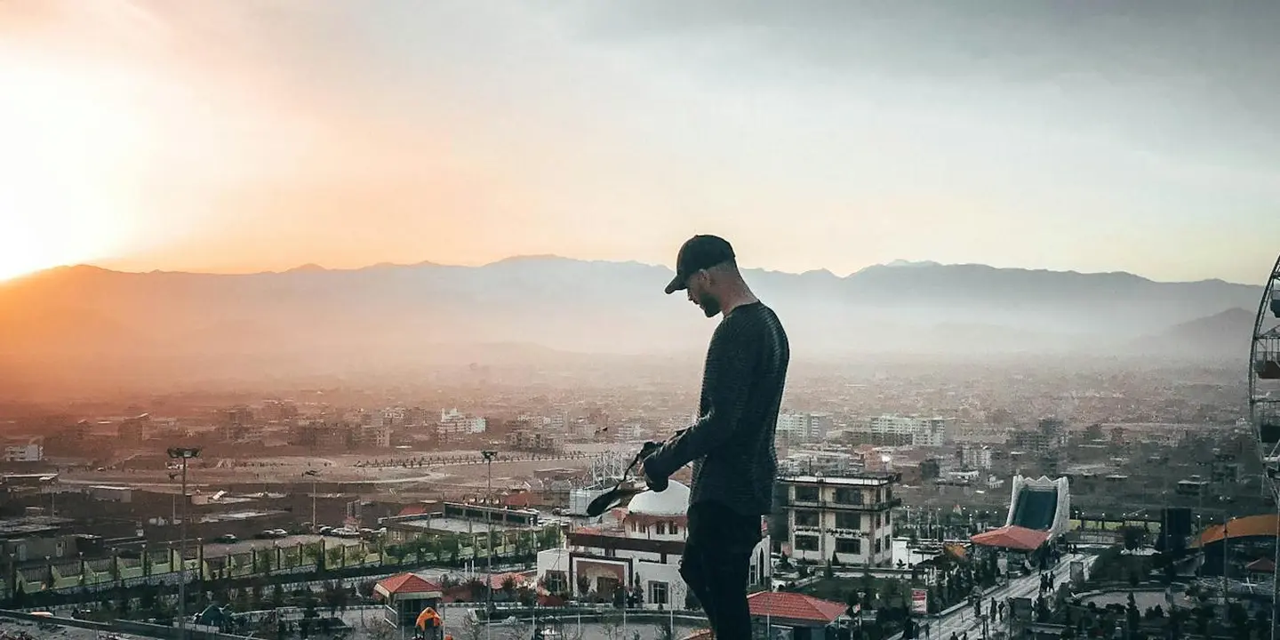 Person standing on a rooftop at sunset, surveying the roof and chimney area with a cityscape in the background.