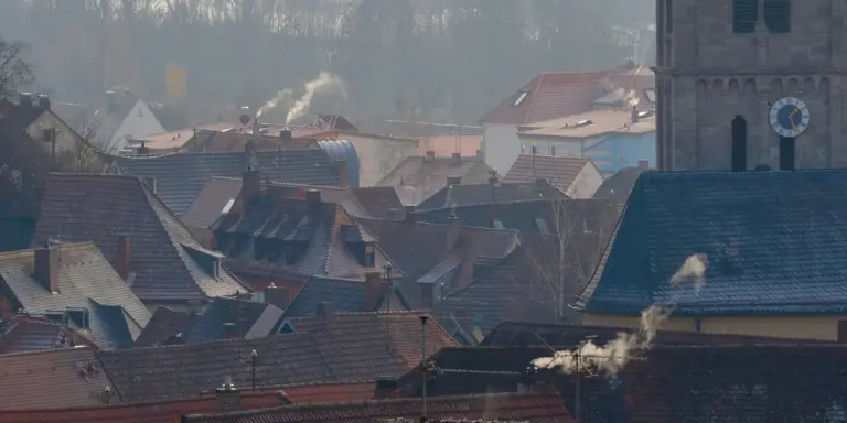 Row of residential rooftops with multiple chimneys emitting smoke.