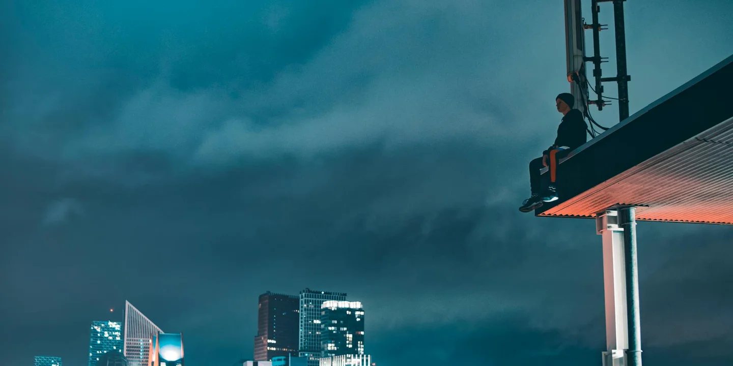 Worker on the edge of a residential roof near solar panels at dusk with a city skyline in the distance.