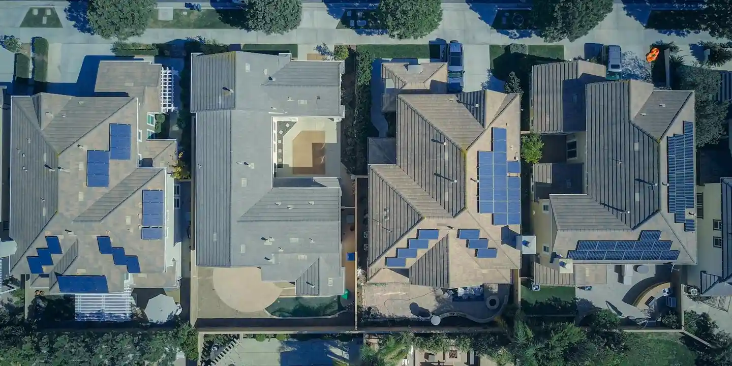 Aerial view of a suburban neighborhood showing multiple houses with solar panels installed on their roofs.