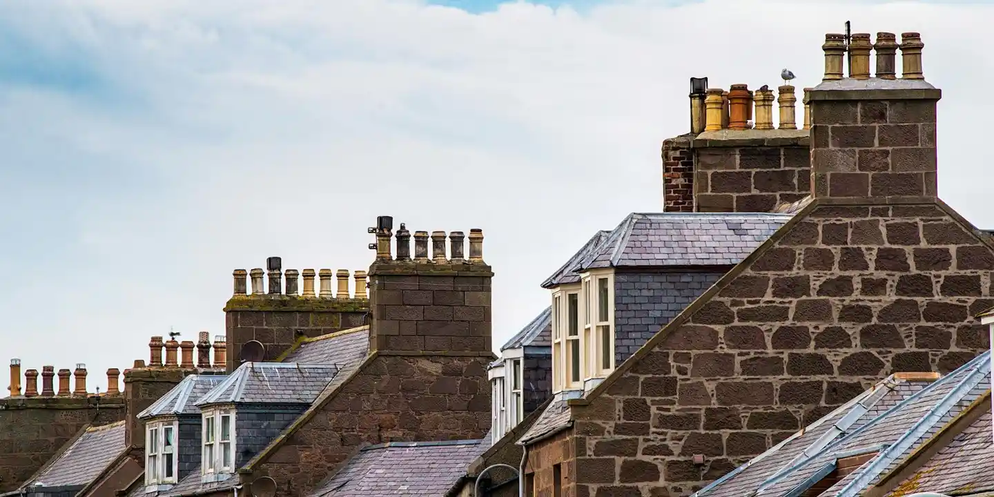 Row of houses with brick chimneys and sloped slate roofs under a blue sky.