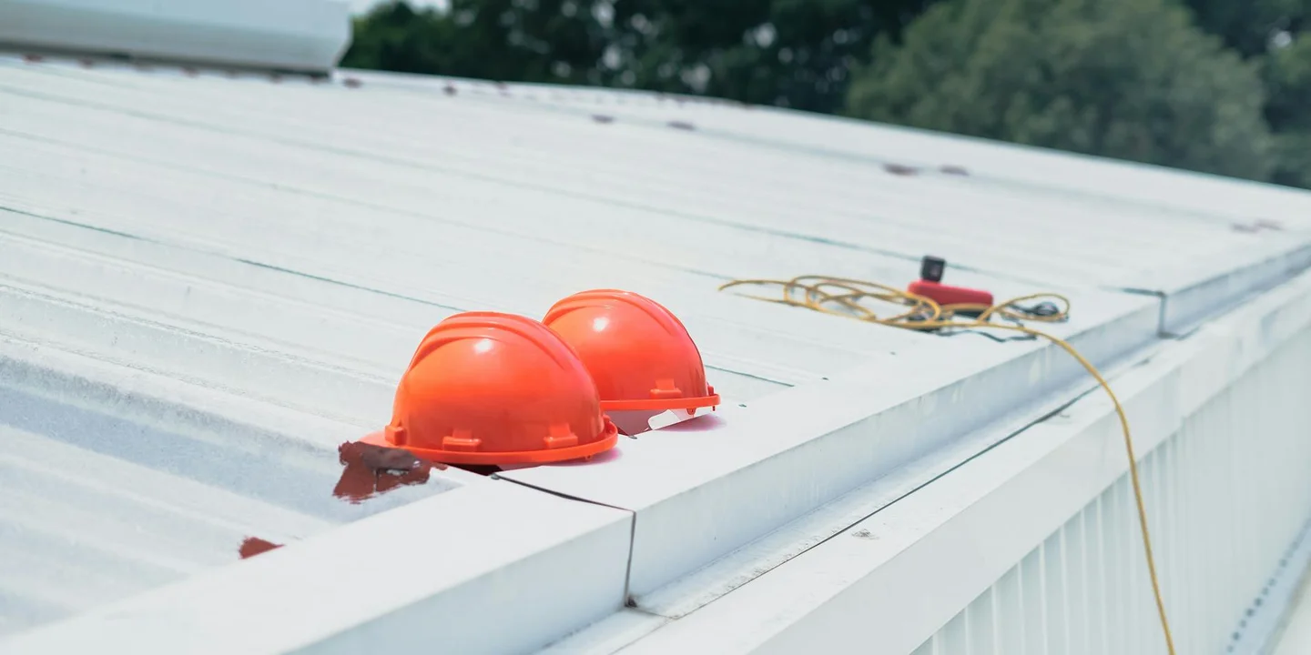 Two red hard hats placed on a white metal roof with a rope and tools in the background, illustrating a roofing installation workspace.