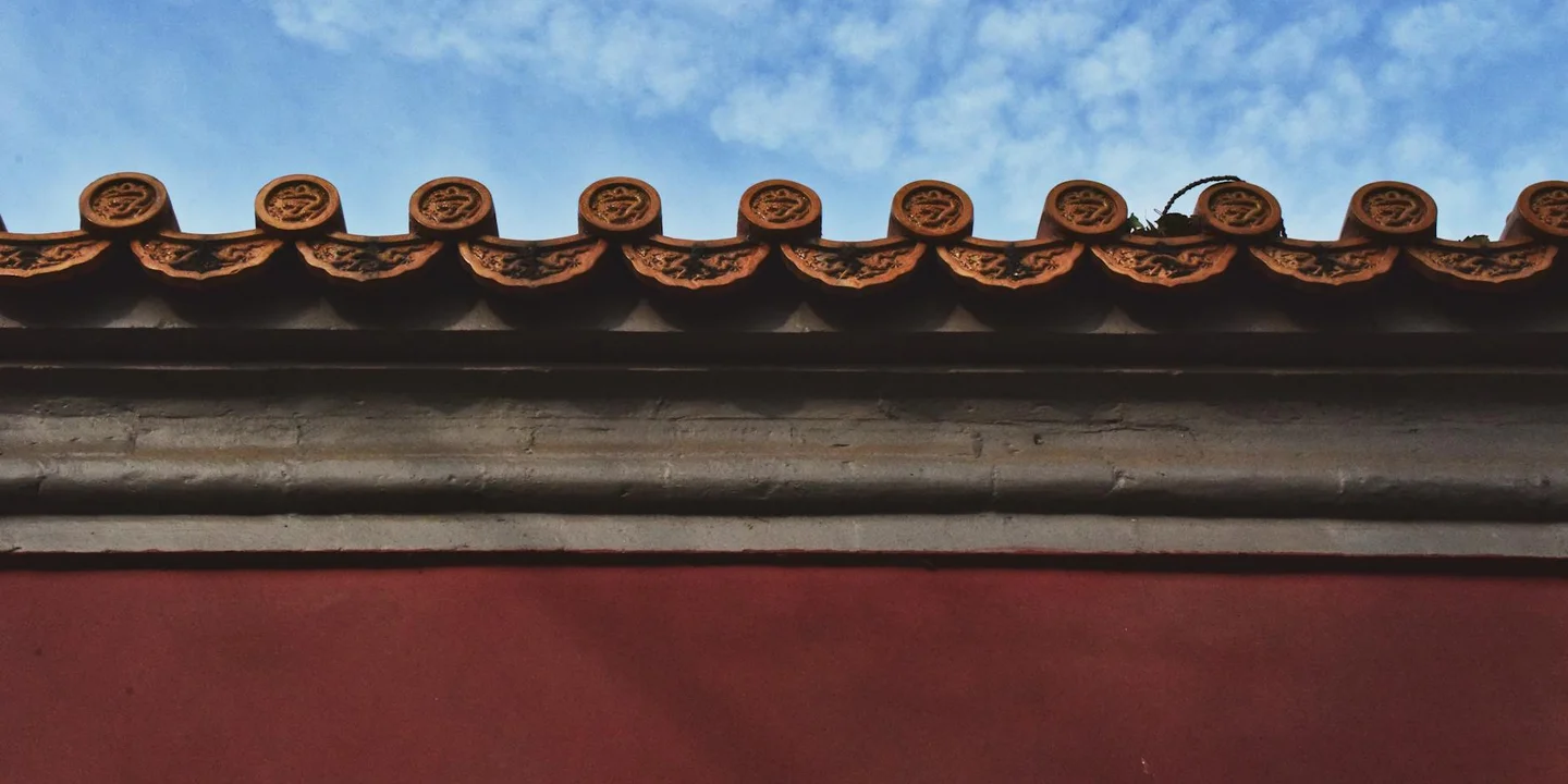 Close-up of terracotta clay roof tiles along the edge of a roof with a blue sky backdrop.