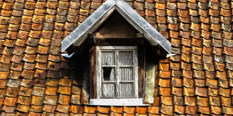 Weathered wooden dormer window set into a slanted tiled roof.