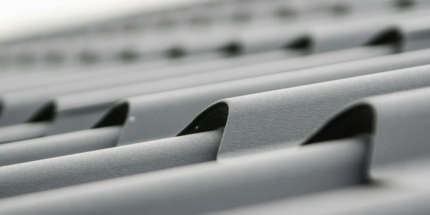 Close-up of overlapping metal roof tiles on a slanted roof, showing gray surfaces and curved tile edges.