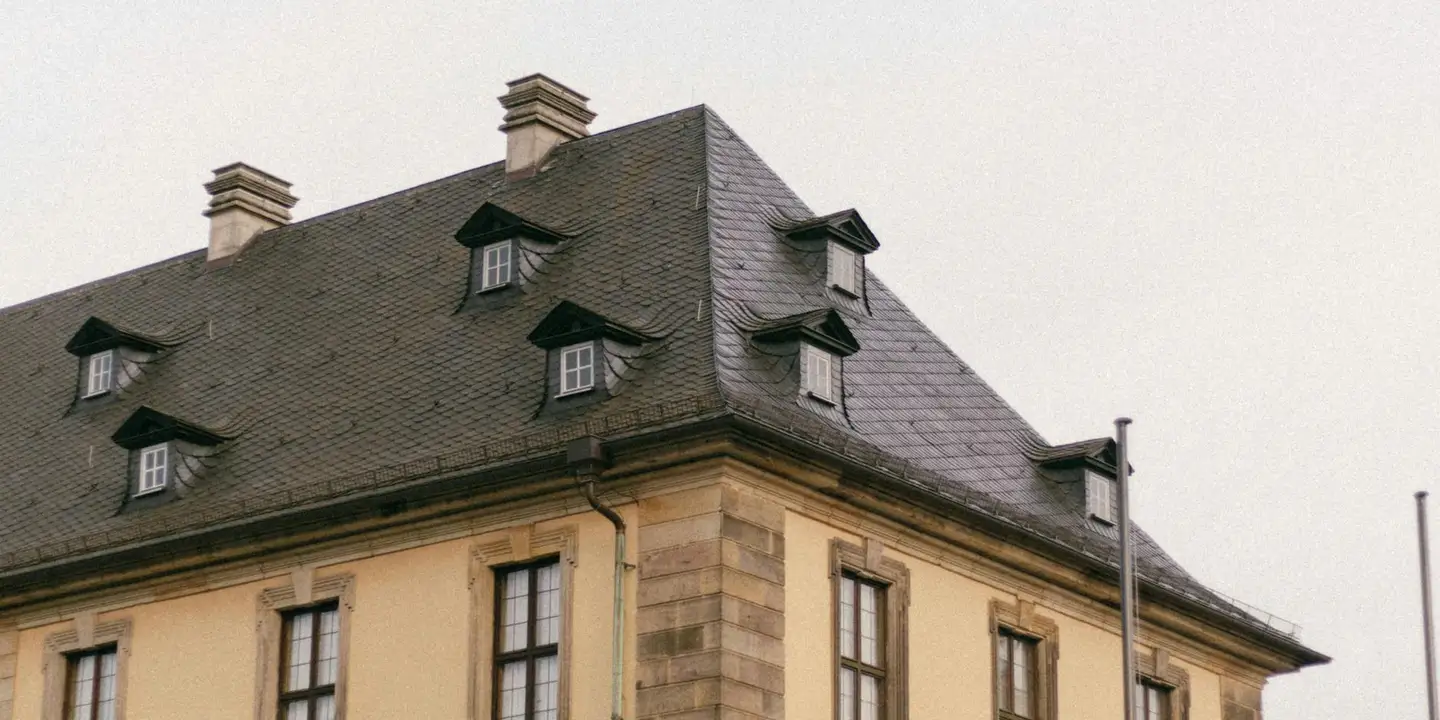 A yellow two-story house with a steep, dark slate roof and several dormer windows.