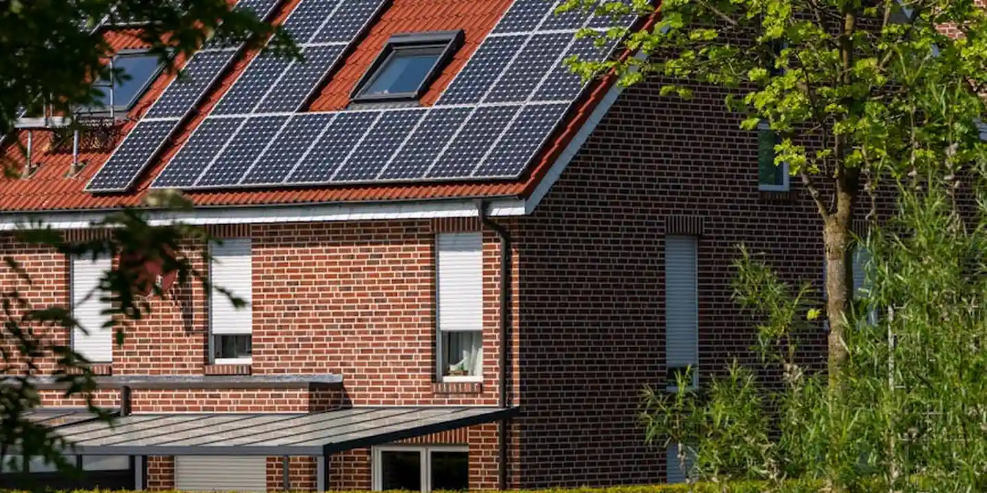 A brick-pitched roof with solar panels mounted along the slope, surrounded by trees.