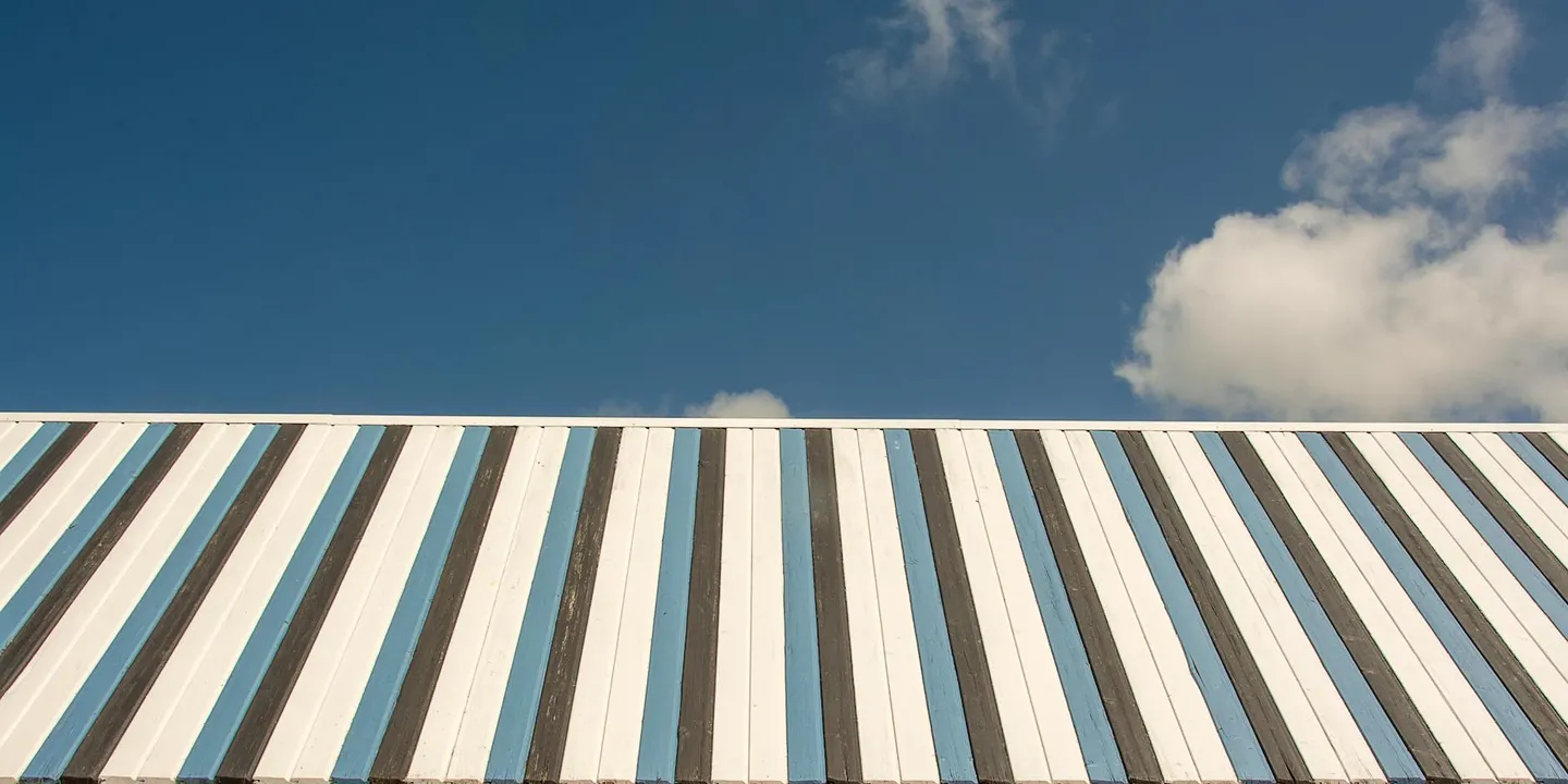 Residential metal roof with blue, white, and gray standing-seam panels under a clear sky.