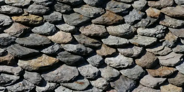 Close-up of layered stone shingles on a roof, showing irregular gray and tan stones.
