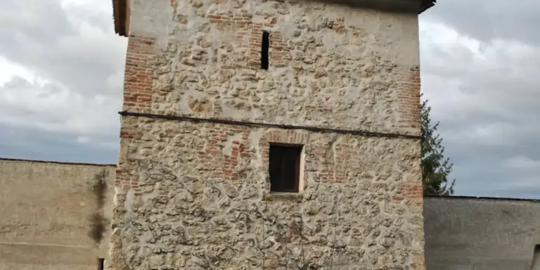 Historic stone tower with a small rectangular window under a cloudy sky.