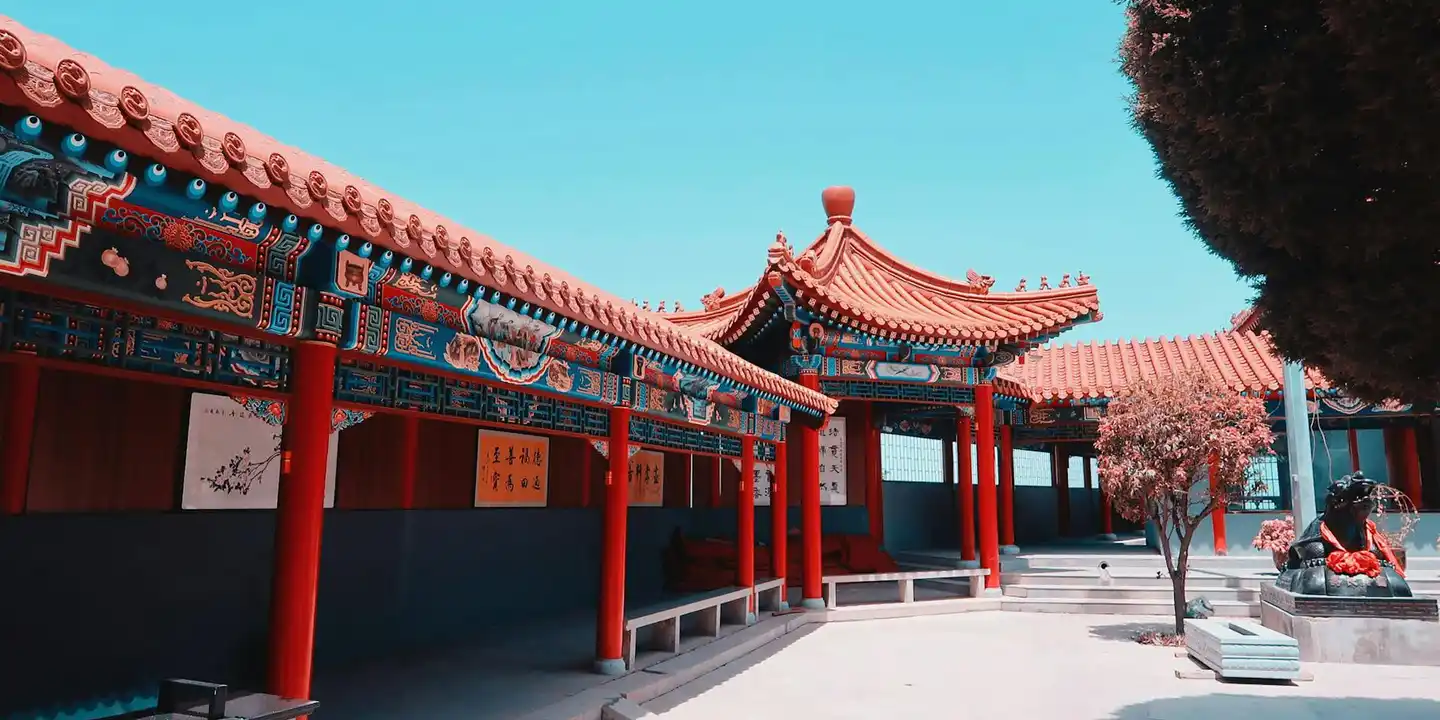 Traditional Chinese temple roof with red columns and decorative eaves under a clear blue sky