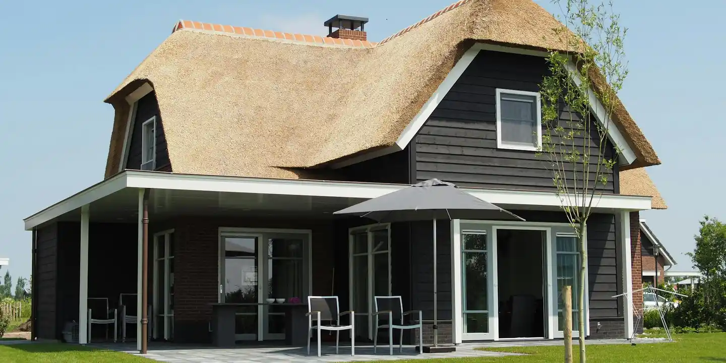 Front view of a house with a thatched roof and a covered patio with outdoor seating.