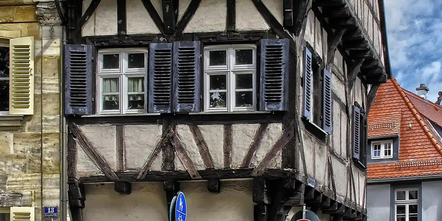 Timber-framed house facade with exposed dark wooden beams, white infill panels, and blue window shutters