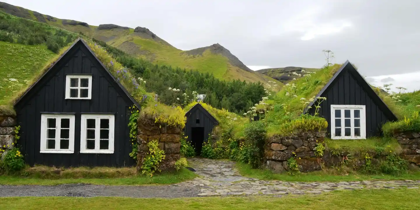 Row of black turf-roofed cottages with white window frames and a stone path in a rural landscape.