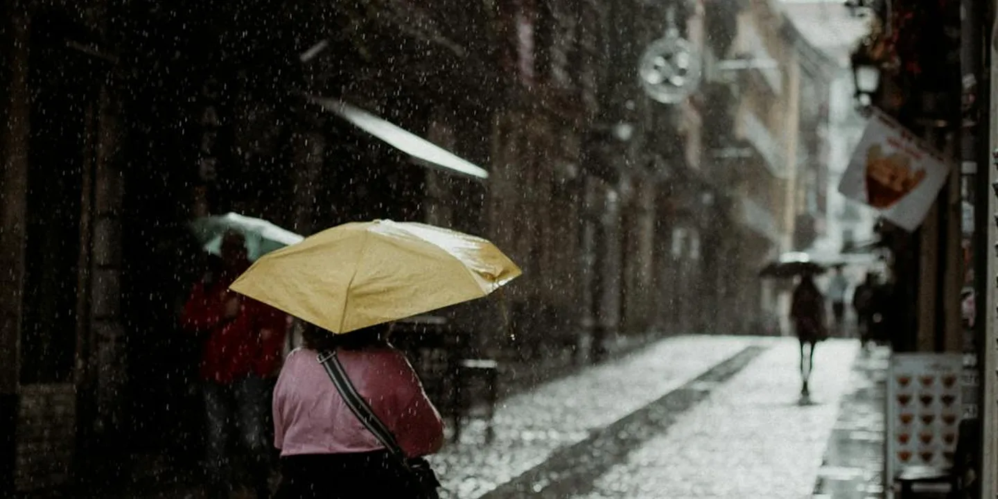 Pedestrian with a yellow umbrella walking in heavy rain on a slick street, illustrating reduced traction and the hazards of wet surfaces.