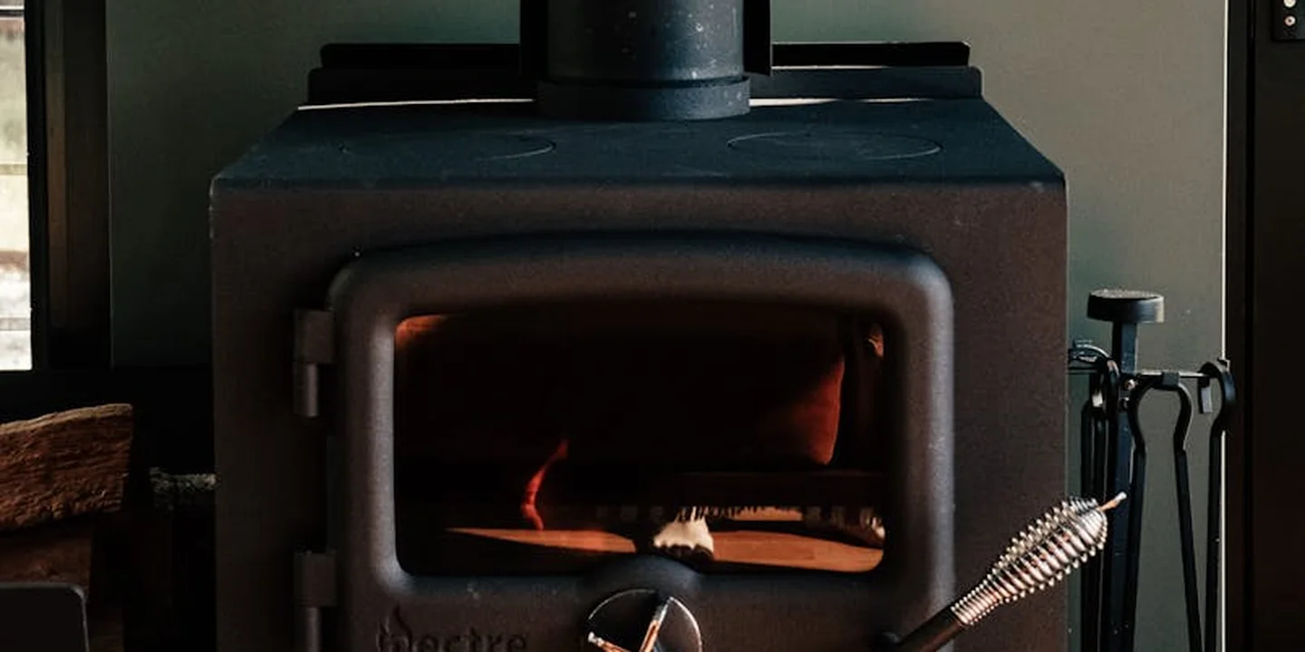 A lit wood-burning stove with a warm glow inside and a set of fireplace tools nearby.