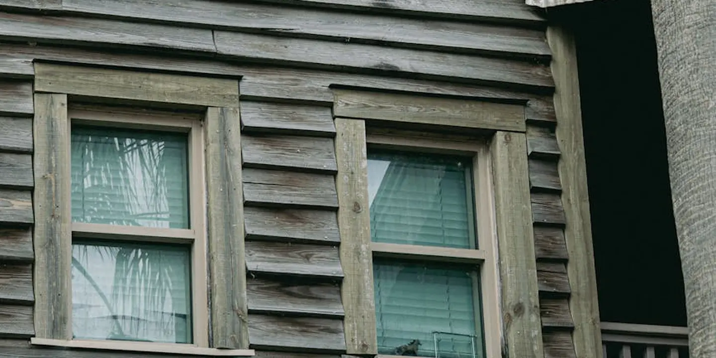 Exterior view of a house with weathered wooden siding and two small windows