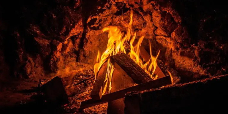 Close-up view of a glowing fireplace with burning logs framed by dark stone interior, illustrating an interior-wall chimney.