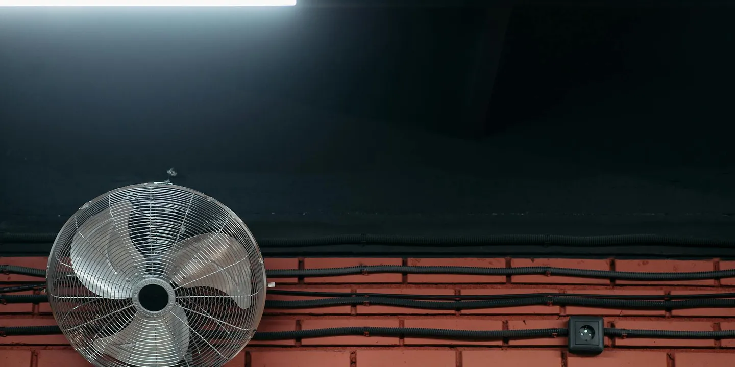Attic ceiling ventilation fan installed in a dark attic with exposed wiring along the wall.