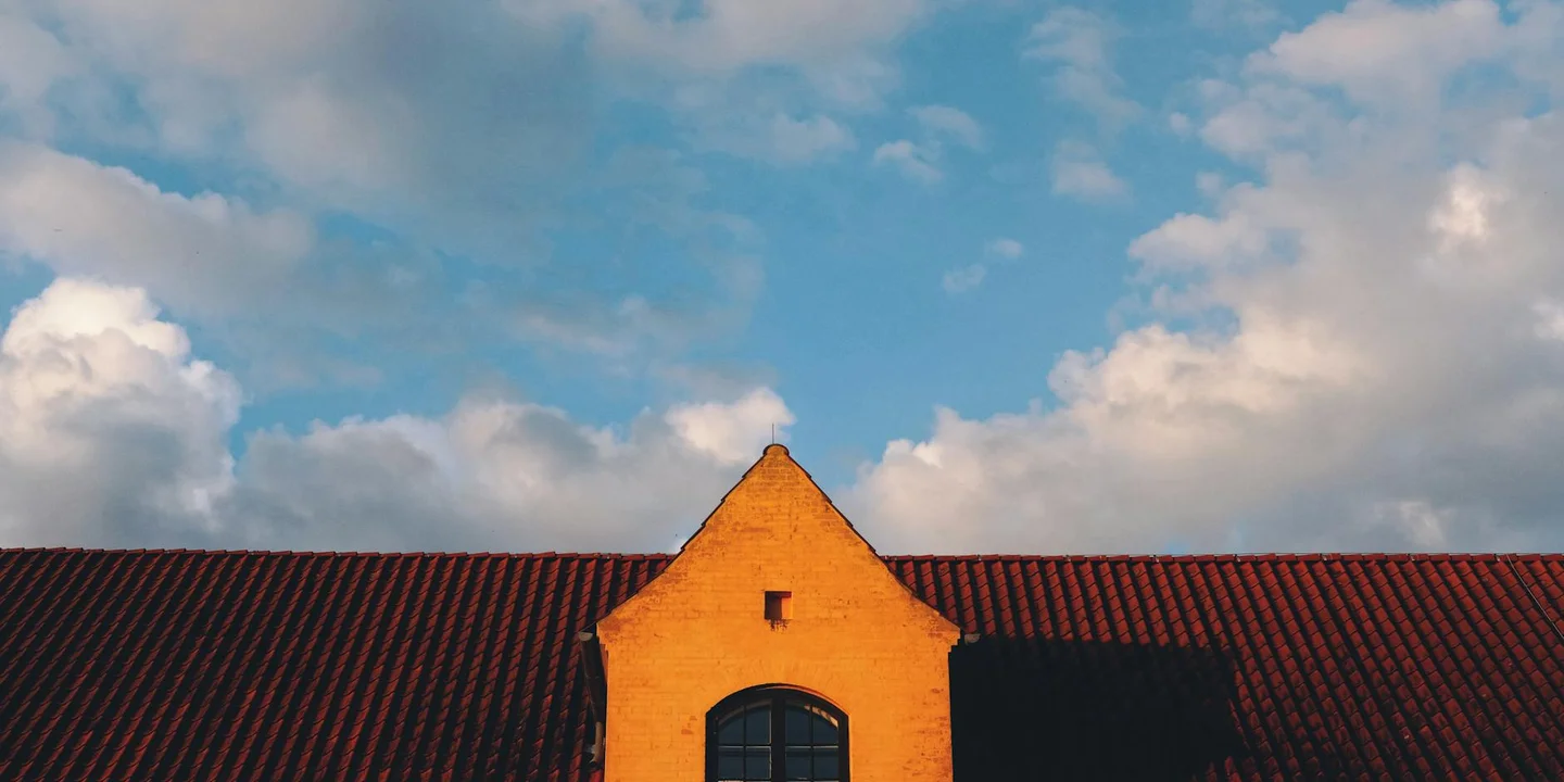 Orange gable wall with a dark roof against a blue sky with clouds.