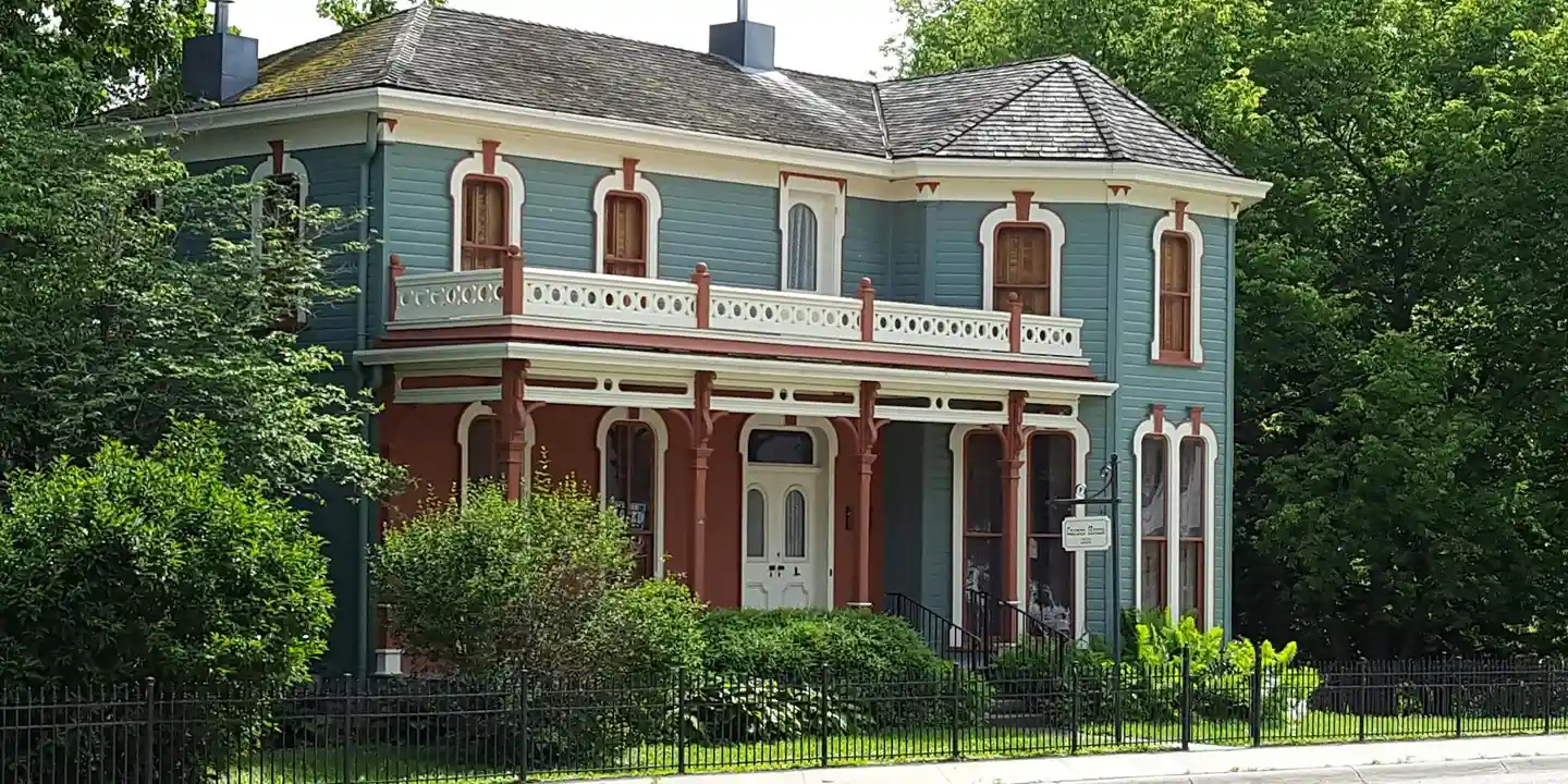 Blue Victorian-style house with a wraparound porch and well-kept greenery.