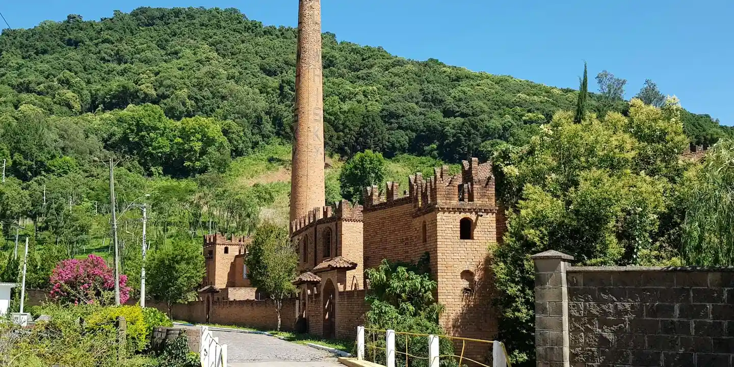 Brick chimney and masonry structures with lush green hills and a clear blue sky in the background.