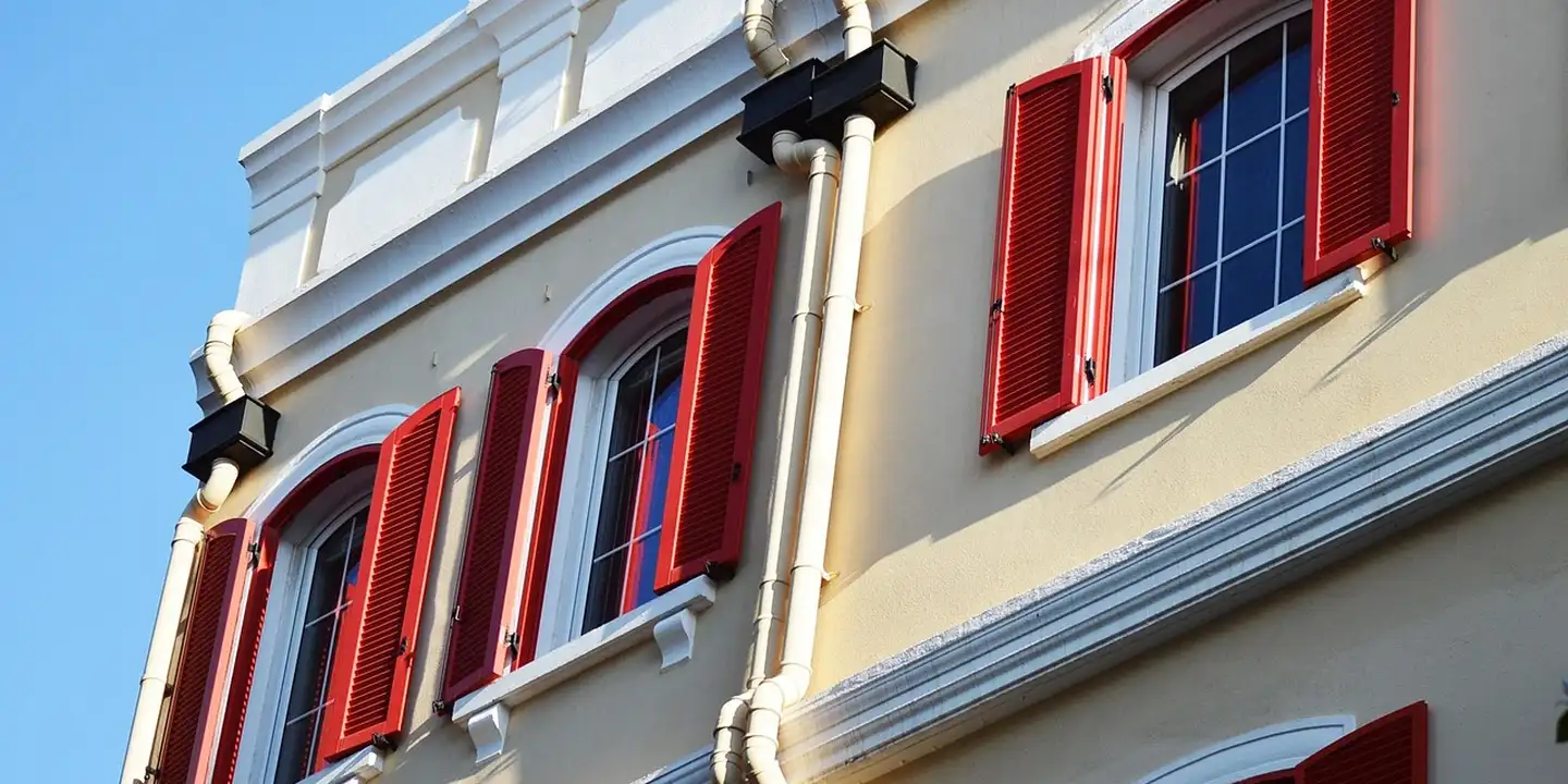 Yellow building facade with red window shutters and white trim