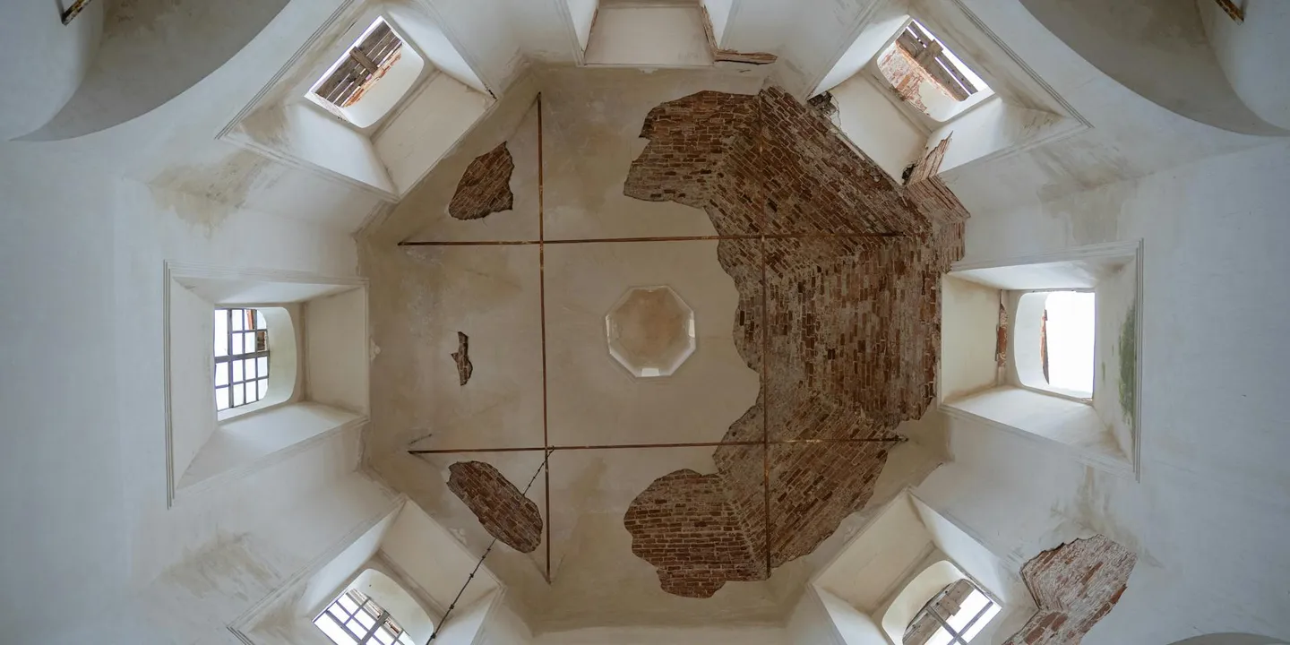 Interior of a vaulted cathedral ceiling with peeling plaster and exposed brickwork near damp patches, visible windows along the sides.