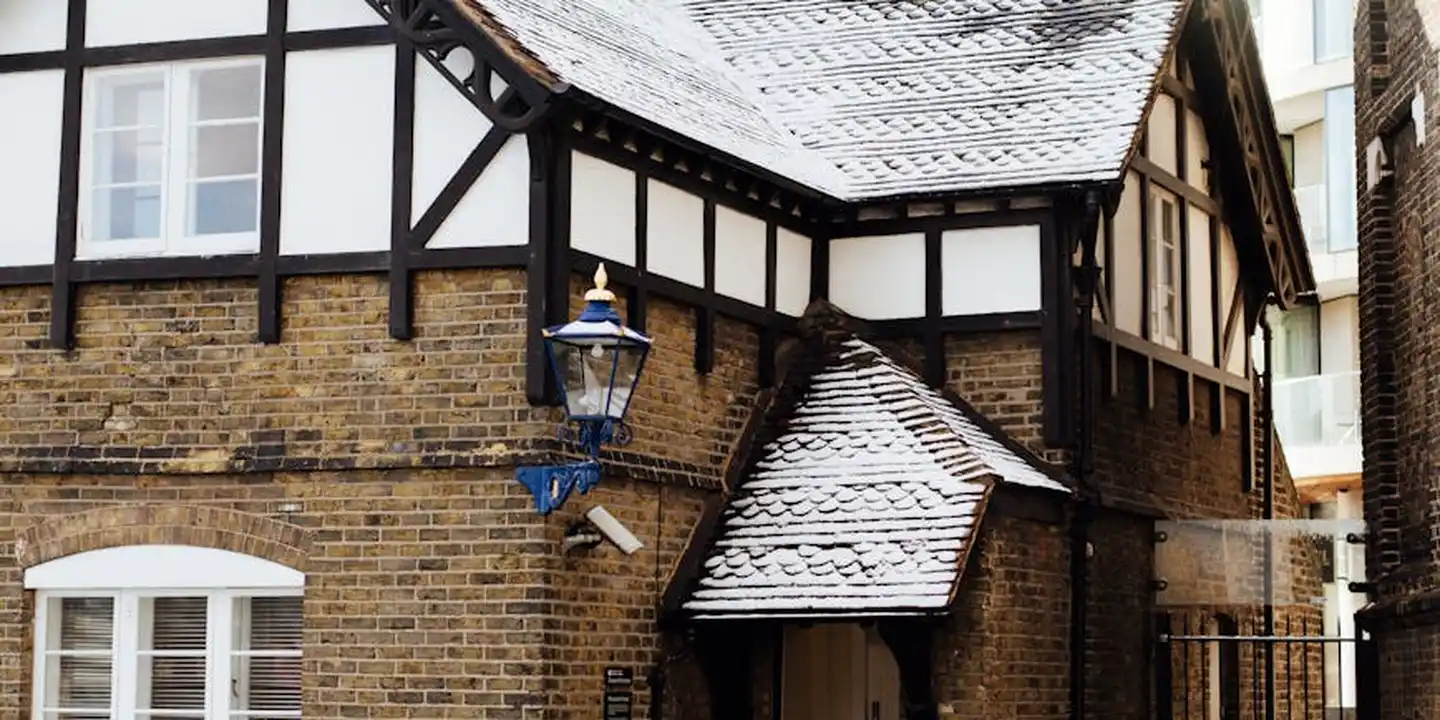 Snow-dusted Tudor-style house with exposed timber framing and brick walls, featuring a blue wall lantern.