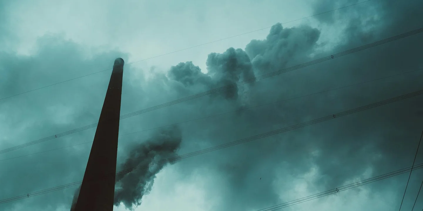 A tall chimney stack exhaling dark smoke into a moody teal sky
