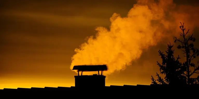 Silhouette of a house chimney emitting a plume of smoke against a golden sunset