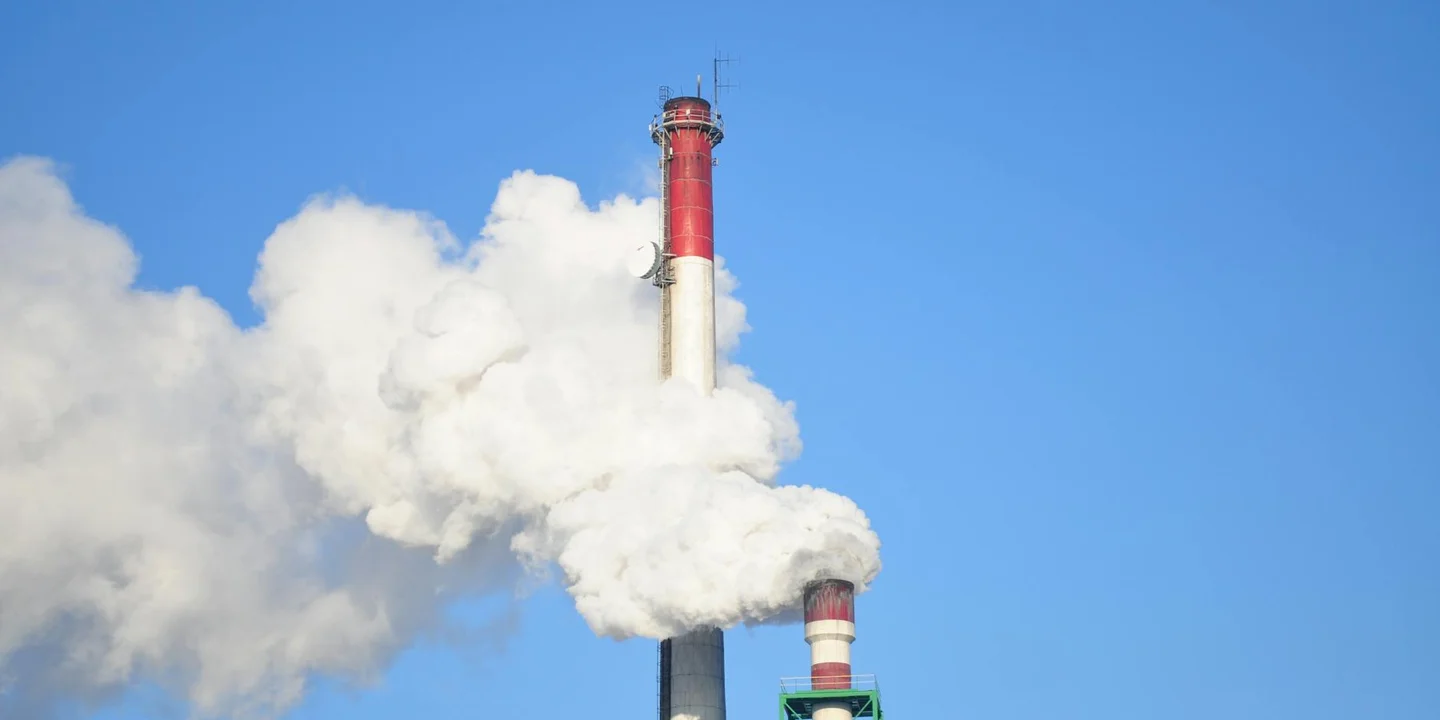 Chimney stack releasing white smoke into a bright blue sky.