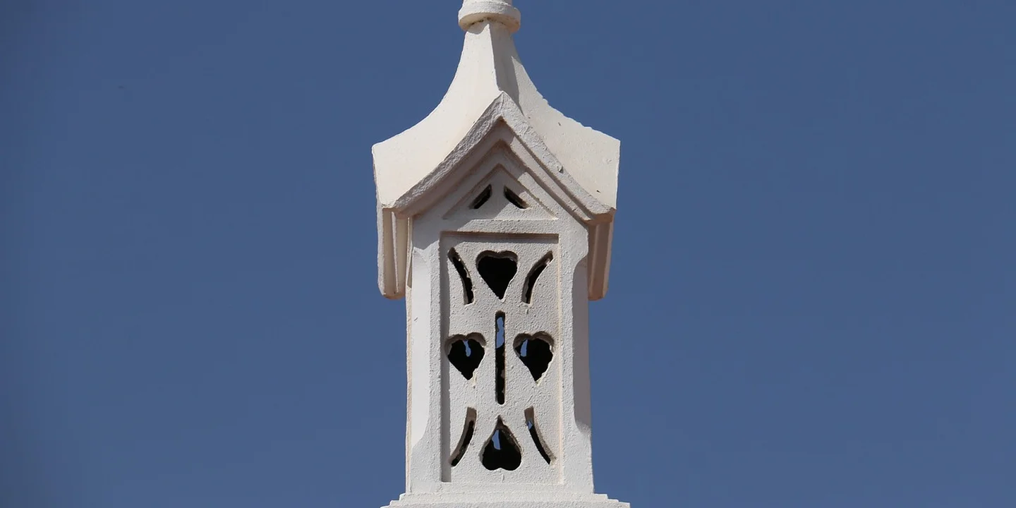 White decorative chimney cap with heart-shaped cutouts against a clear blue sky.