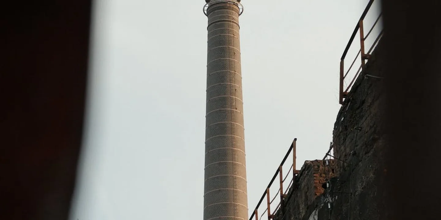Interior view of a tall chimney flue rising inside a building, with brick walls and a metal railing nearby.