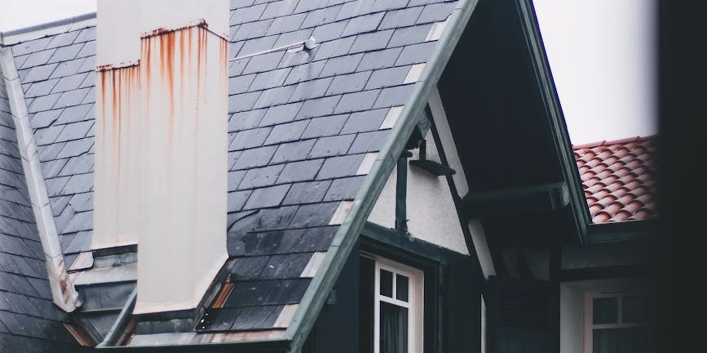 A sloped roof with two chimneys; one metal chimney shows rust staining, illustrating potential hazards and questions around chimney heat reclaimers and flue heat exchangers.
