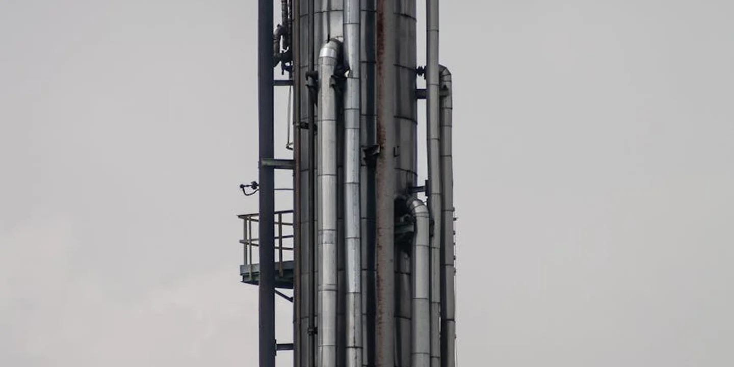 Tall industrial chimneys and connected flue pipes with a platforms and ladders at a processing facility