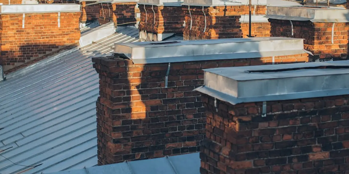 Brick chimneys rising from a metal roof, illustrating traditional chimney structures that can be monitored by smart sensors.