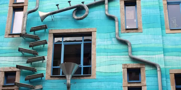 Exterior turquoise building with multiple metal gutters and downspouts