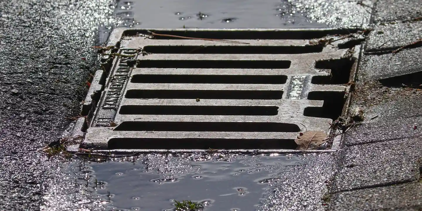 Metal street drainage grate with water puddles on asphalt