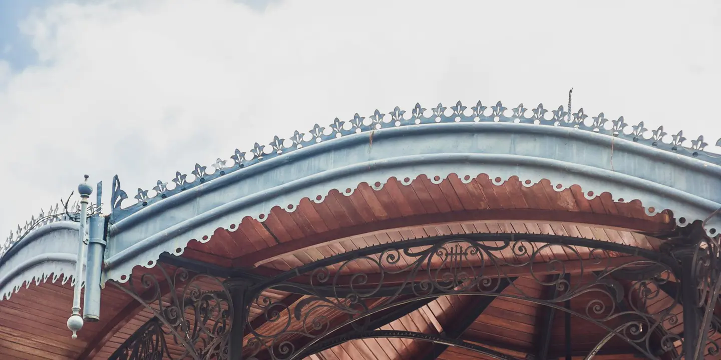 Close-up of an ornate gazebo roof with decorative wrought-iron trim and curved wooden panels.