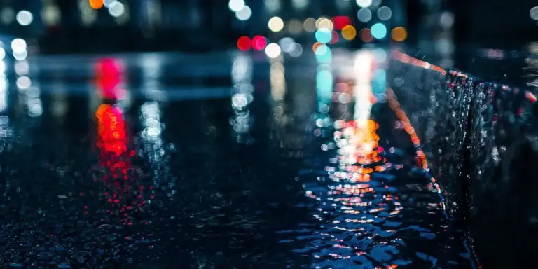 Rain-soaked street with a gutter edge and colorful reflections, illustrating the importance of gutter guards.