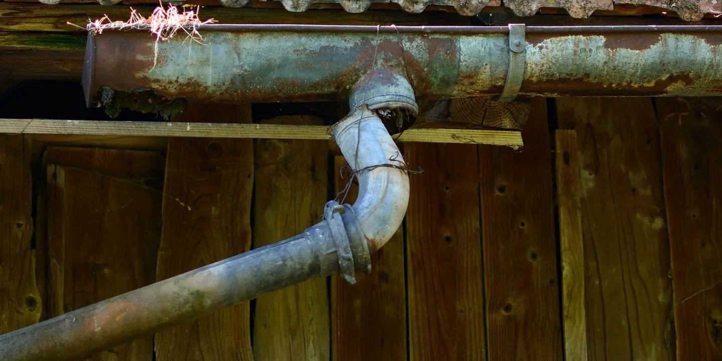 Close-up view of a rusted metal gutter joint against a wooden exterior wall, illustrating installation details and corrosion